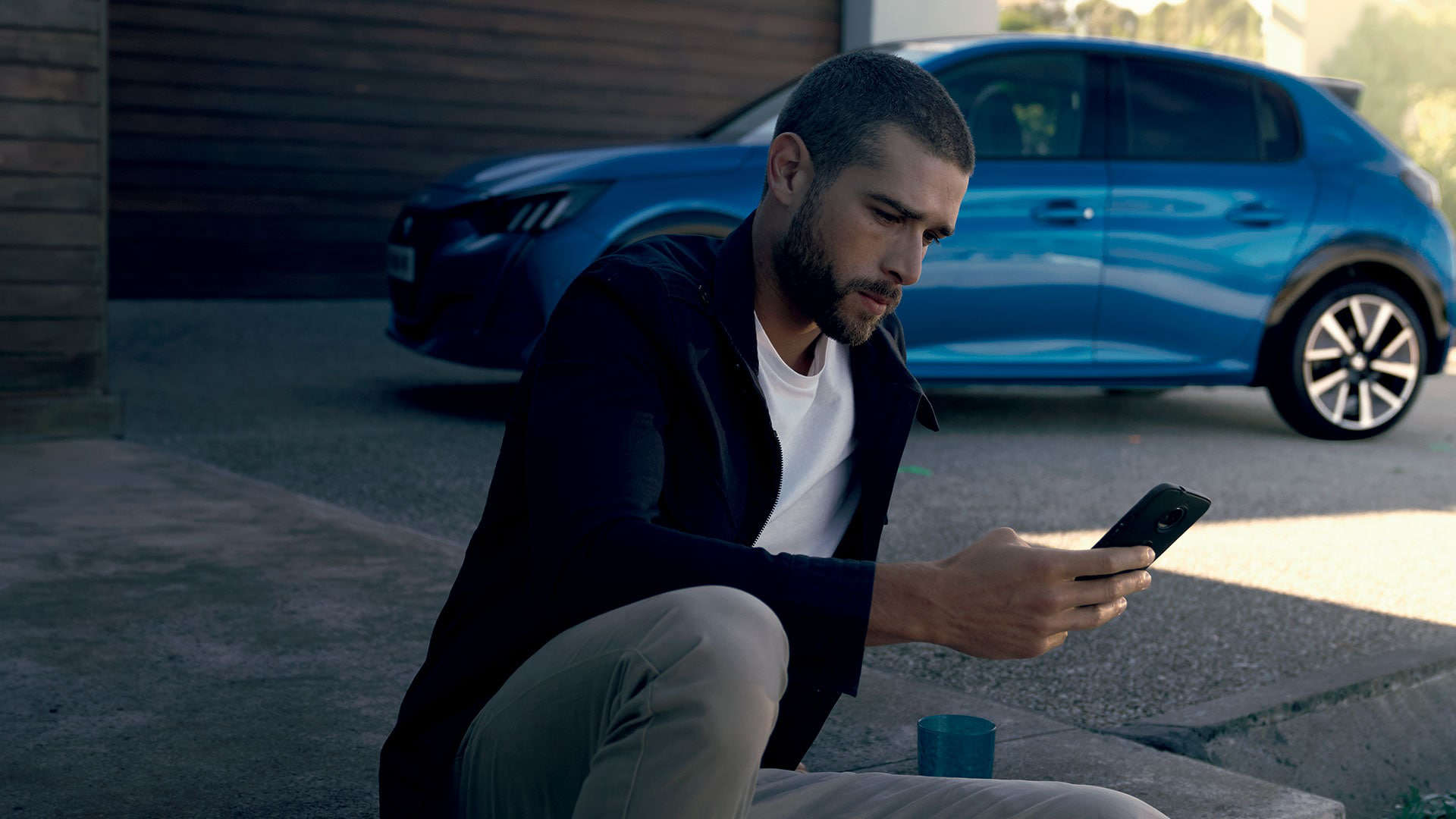 Чоловік дивиться на екран смартфона біля автомобіля Peugeot