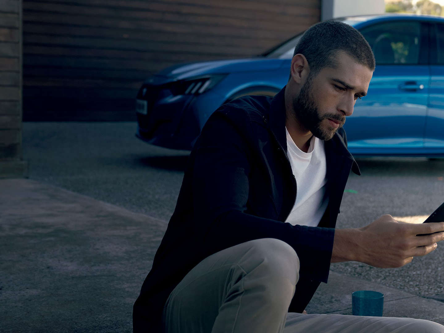 Чоловік дивиться на екран смартфона біля автомобіля Peugeot